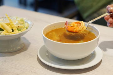 A white bowl of hot and sour yellow curry paste soup with shrimp and green papaya served with fresh mixed vegetable, Southern Thai traditional food.