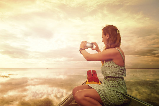 Woman traveller photographing on smartphone a sunset, enjoying calm tropical sea