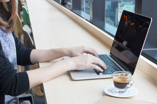 woman typing on laptop keyboard with a cup of coffee on wooden desk.