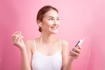 Happy asian girl dancing and listening to the music isolated on a pink background