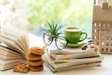 Coffee cup, open book, glasses, cookies and flower on window sill. Reading and breakfast concept - obrazy, fototapety, plakaty