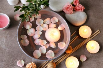 Beautiful spa composition of flower petals with water in bowl and candles on gray background