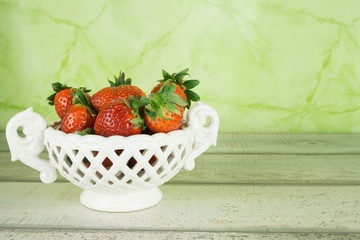 Viele frische Erdbeeren, einige in einer weißen Porzellanschale, grüner Hintergrund,  Textfreiraum,