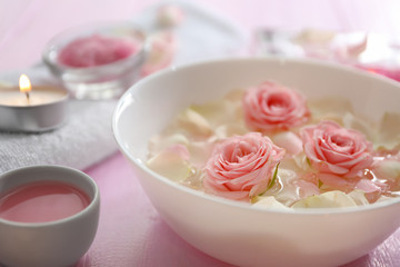 Bowl with flower petals on water on wooden table, closeup