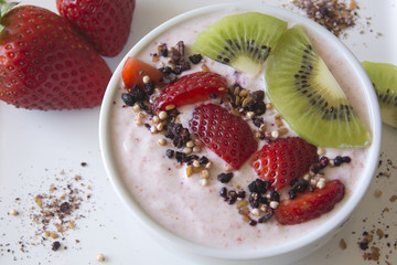 Greek strawberry yoghurt served in a bowl with fresh strawberries, kiwis and a superfruit topping of dried blueberries, hibiscus, chia seeds and airy quinoa pops