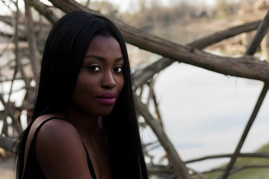 Beautiful sight. Black model looking at the camera with branches and river behind her.