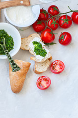 Fototapeta na wymiar Set of ingredients for bruschettas with goat cheese, pesto sauce and tomatoes abd baguettes on a white stone background. Top view and copy space.