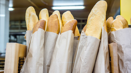 Fresh baked rustic bread loaves in paper bags on wooden shop shelf