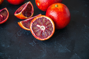 Whole and slices of blood oranges on a black slate background. Copy space and close up.