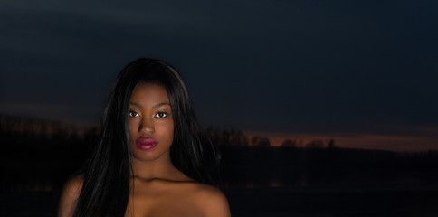 Black model close up. Sunset and darkness in the background with a black girl glowing in it