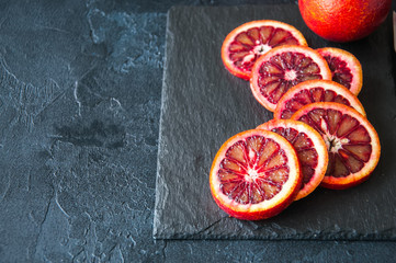 Whole and slices of blood oranges on a black slate background. Copy space and close up.