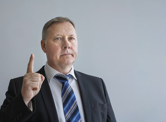 серьезный представительный мужчина указывает рукой вверх указательным пальцем