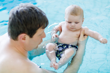 Happy middle-aged father swimming with cute adorable baby in swimming pool.