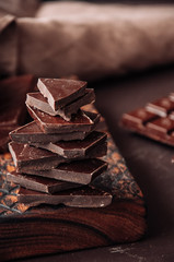 Pieces of dark chocolate on a wooden board at monochrome setting. Toned.