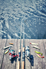 Retro toned picture of fishing equipment with artificial spinning lures on a wooden pier.
