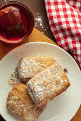 Three puff pastries in a white plate with cup of red fruit tea on a wooden table, top view, selective focusing, vertical
