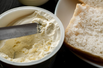 Cream cheese in plastic jar with knife in it closeup shot, selective focus