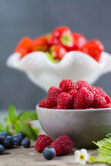 Fresh organic summer berries - ripe raspberry, strawberry, blueberry with leaves on wood background