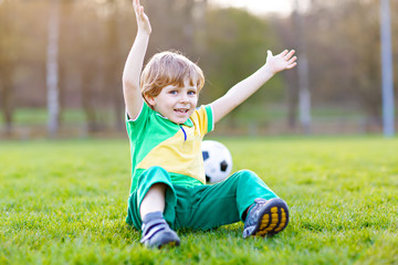 Little cute kid boy of 4 playing soccer with football on field, outdoors