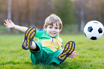 Little cute kid boy of 4 playing soccer with football on field, outdoors