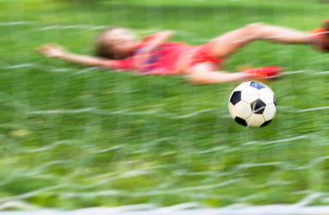 Boy is playing football in summer time, kid kicks  ball into football gate, child felt down playing soccer, the ball flies into the net