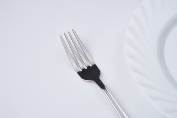 Empty white dinner plate with silver fork isolated on white background with copy space. Table Setting