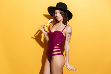 Young girl in swimsuit holding banana and looking at camera