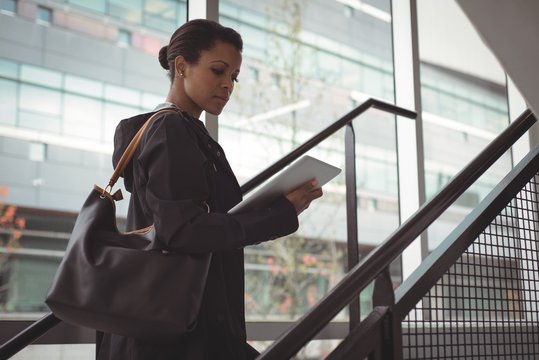 Businesswoman holding digital tablet while standing on staircase in office