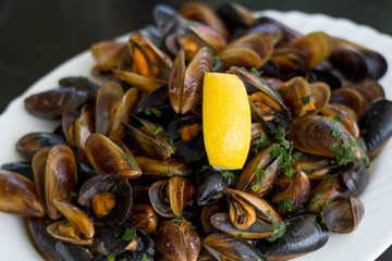 Shellfish mussels with lemon and herbs on a white plate. Seafood.
