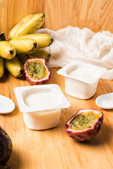 Plastic cups with yogurt on wooden background Breakfast with bananas,  passion fruits and yoghurt. White spoon and napkin on table. 