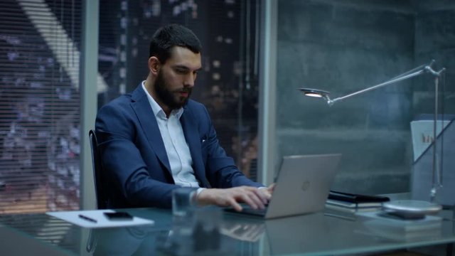 Late at Night Businessman Works on a Laptop in His Private Office with Big City Window View. Shot on RED EPIC-W 8K Helium Cinema Camera.