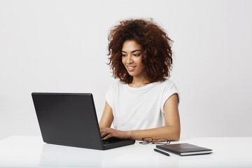 African businesswoman smiling working at laptop over white background. - Powered by Adobe