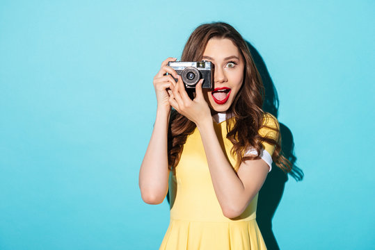 Portrait of a cheerful girl in dress using retro camera