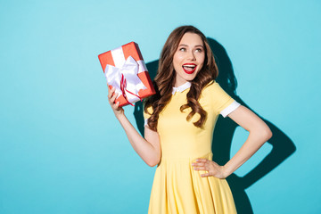 Playful girl in dress holding gift box and looking away