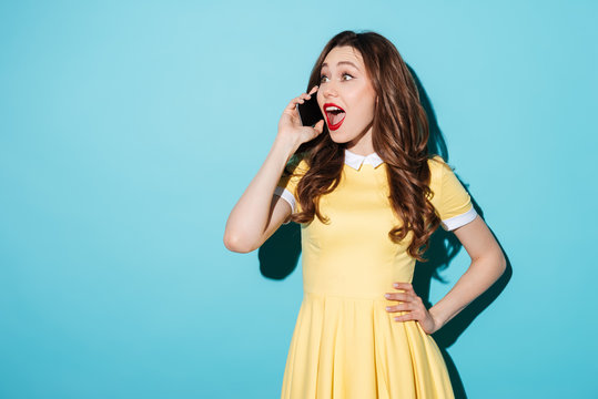 Happy young brunette woman in yellow dress talking by phone.