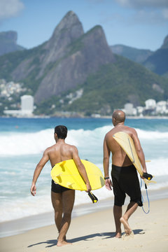 Young Brazilian surfers walking with their surfboards from Arpoador, the popular surf spot, toward Ipanema Beach, under the backdrop of Two Brothers Mountain in Rio de Janeiro, Brazil