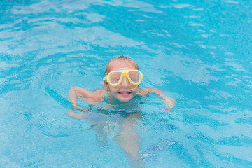 Naklejka premium Cute happy young girl child relaxing on the side of swimming pool wearing pink goggles