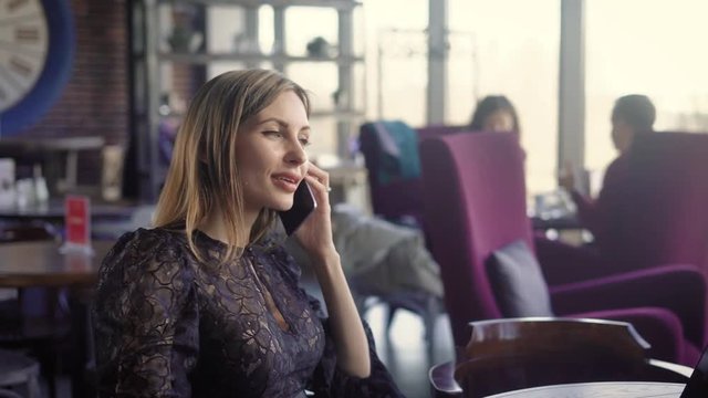 Beautiful smiling female talking phont. Young smiling female in elegant dress talking phone while sitting in cafe.