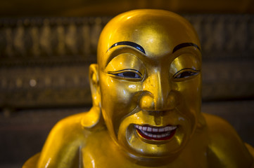Head and shoulders close up of the smiling face of a golden seated Buddha in a Buddhist temple in...