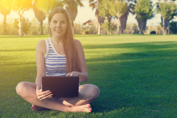 Young woman sitting on green grass and meditating with laptop