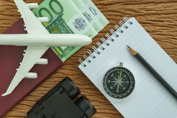 Travel planning concept with airplane, passport, compass, binoculars, pencil, paper note and Euro banknotes on wood table