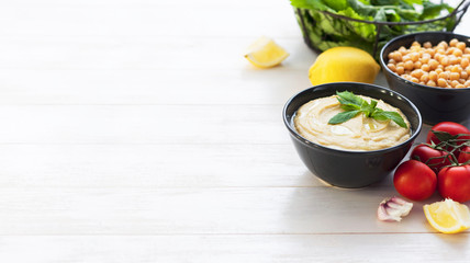 Bowl with hummus, chickpeas, lemon, cherry tomatoes and herbs on a white rustic wooden background.
Middle Eastern cuisine. Background hummus with place for text.