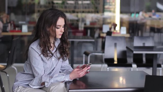 Beautiful young woman while in the cafe uses her mobile device