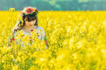 Beautiful young woman in Ukrainian embroidered standing in a field of yellow rape flowers