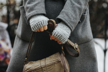 A girl in a coat and knitted gloves is holding a leather bag. Close-up of hands. A woman expects, nervous. Compressed hands, beautiful manicure