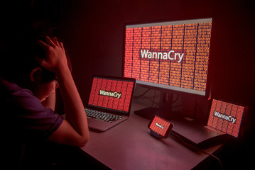 Young Asian male frustrated, confused and headache by WannaCry ransomware attack on desktop screen, notebook and smartphone, cyber attack internet security concept