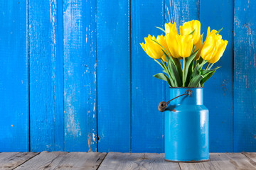 Bouquet of yellow tulips in vase on a blue background