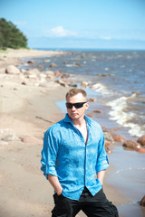 A young man, a guy in an open blue shirt on a summer day's beach
