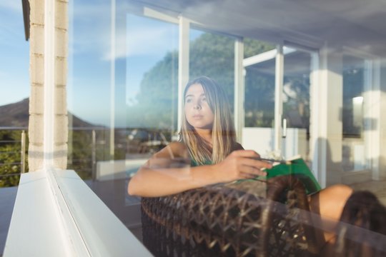 Thoughtful woman relaxing on chair and looking through window