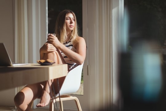 Woman relaxing on chair while holding coffee cup at home